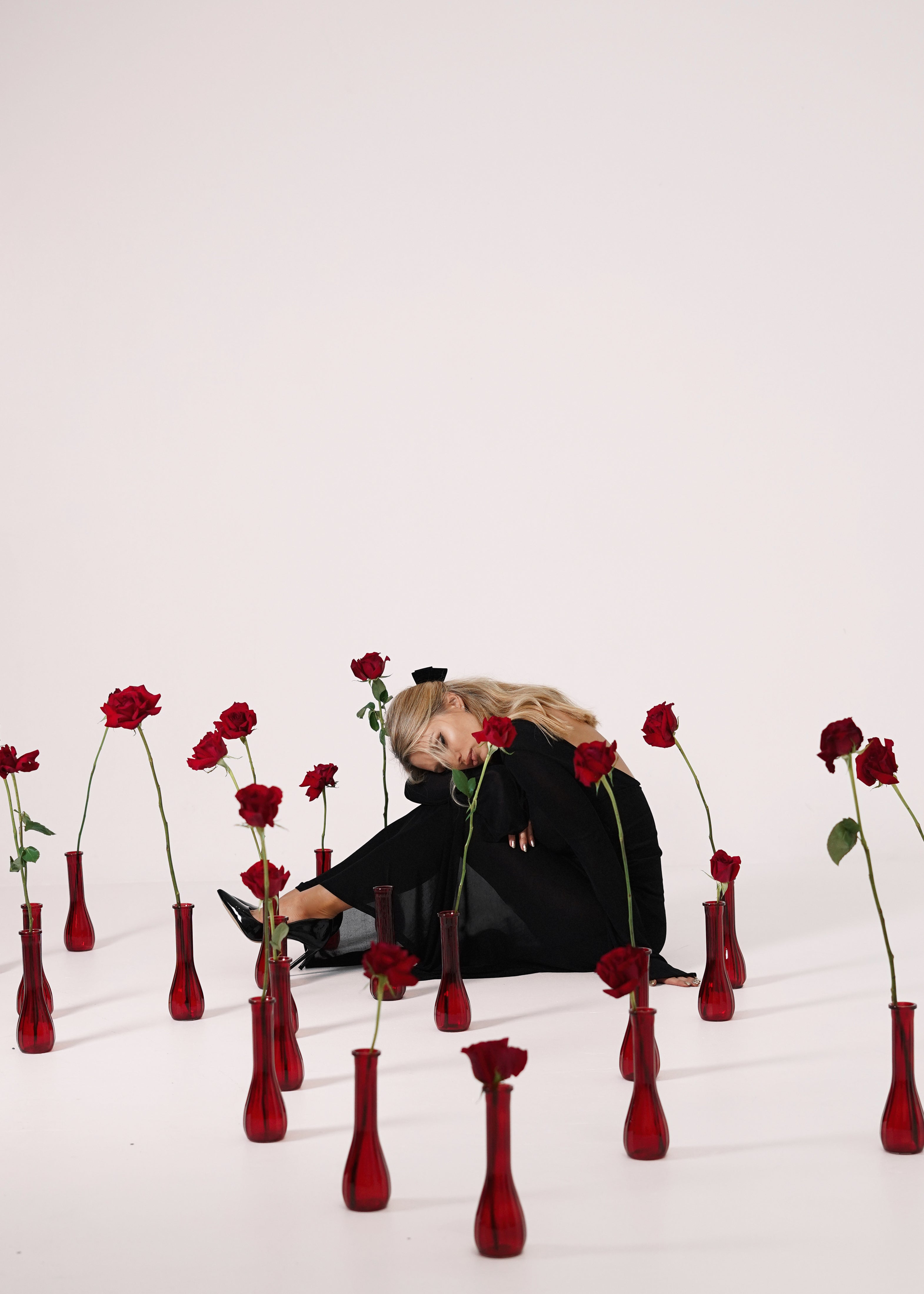 Girl in black dress sitting around bud vases with red roses