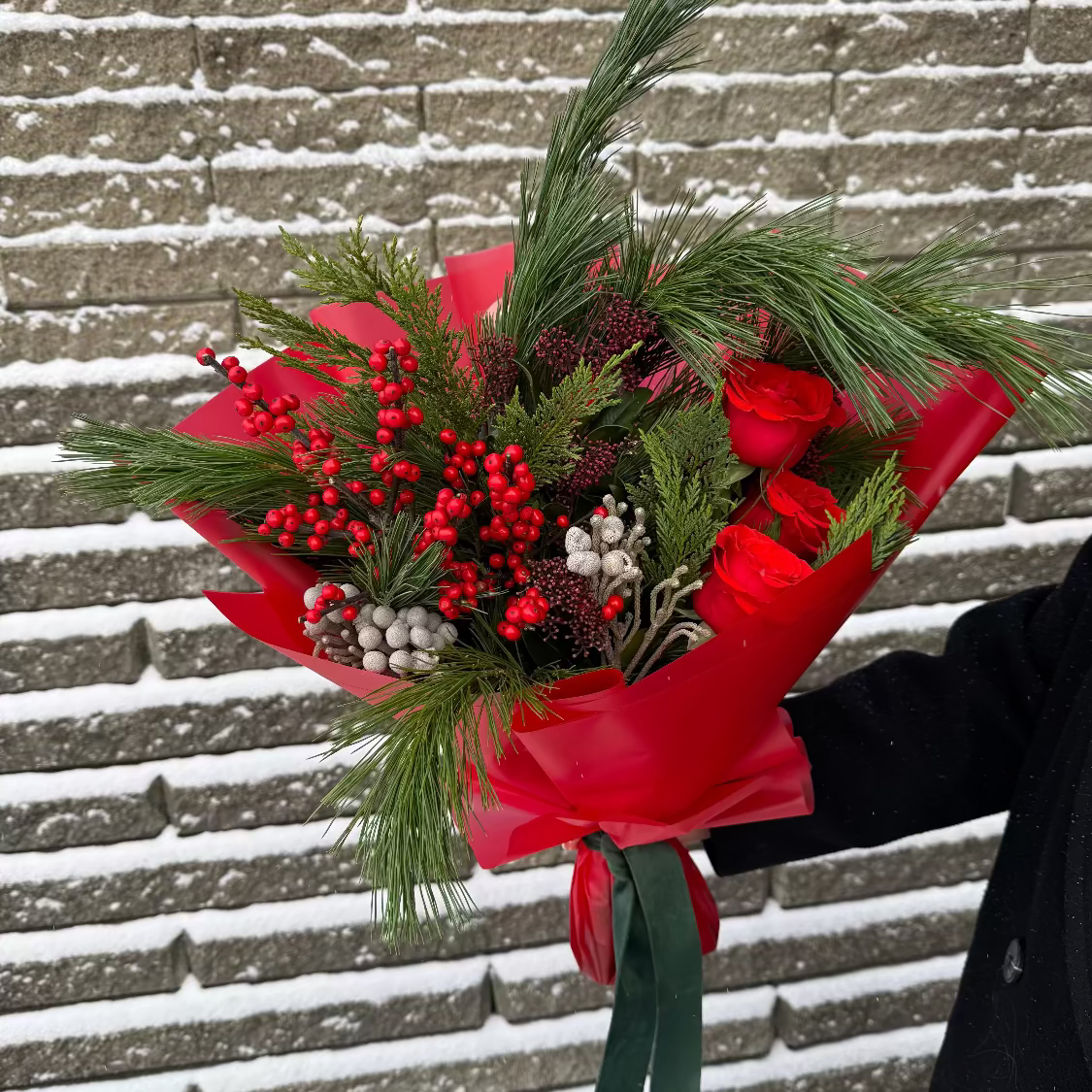 Bouquet of flowers with evergreens and velvet ribbon against a snowy brick wall.