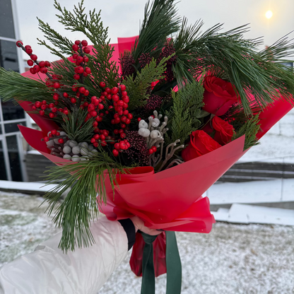 Bouquet of flowers with evergreens and velvet ribbon against a snowy brick wall.
