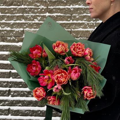 Person holding a bouquet of pink and orange tulips against a snowy brick wall.