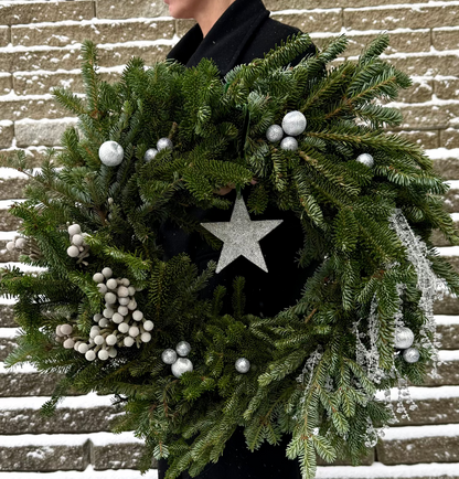 Green wreath with white berries and a star ornament against a snowy brick wall.