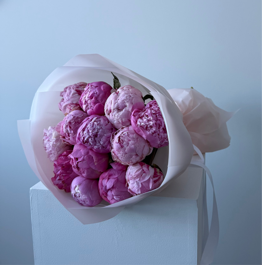 Bouquet of pink flowers wrapped in white paper on a light blue background