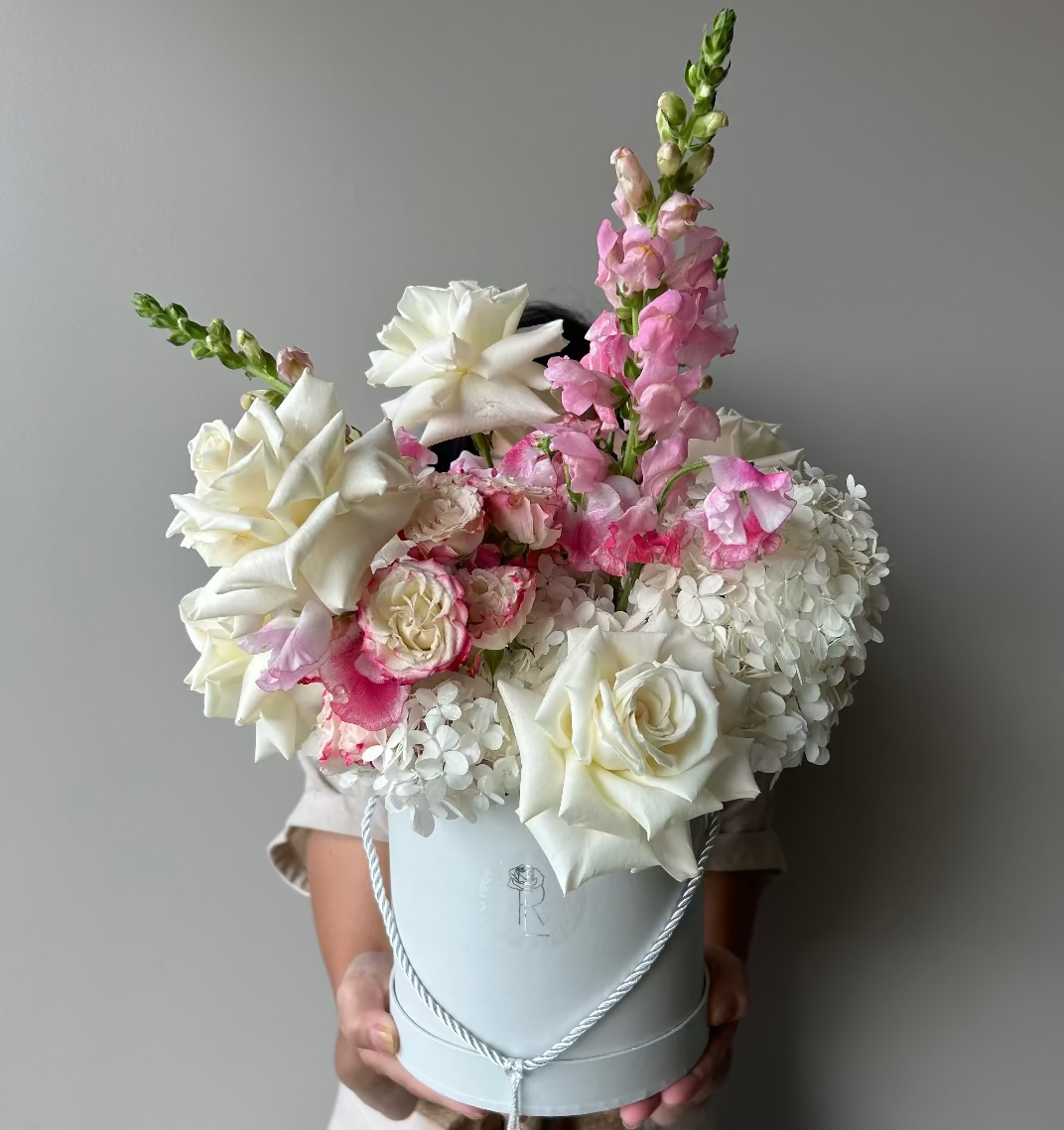 Floral arrangement in a white box held by a person against a gray background