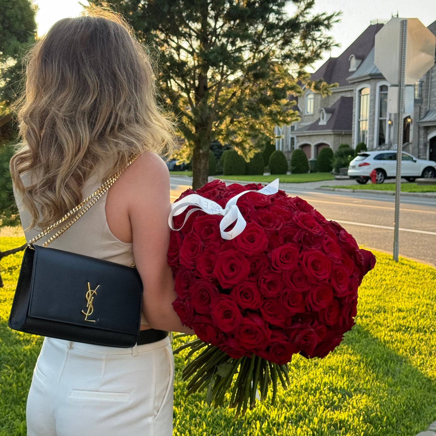 Person holding a large bouquet of red roses and a black handbag with a gold chain.