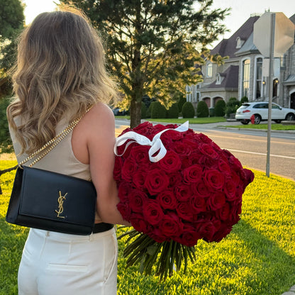 Person holding a large bouquet of red roses and a black handbag with a gold chain.